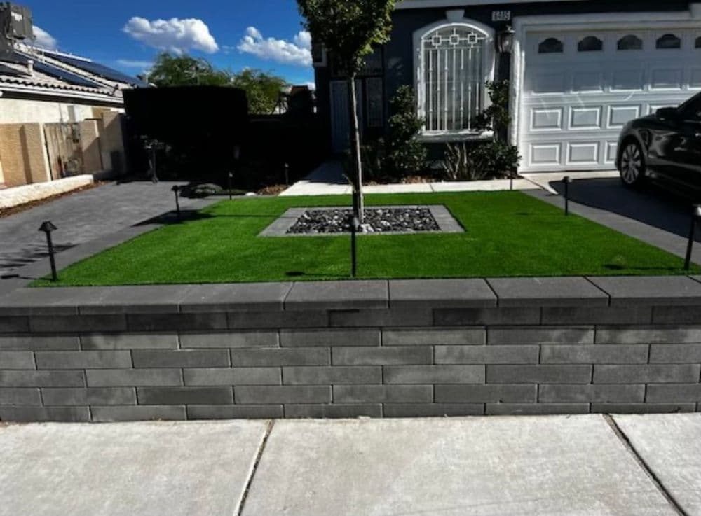 Modern front yard design featuring artificial grass, decorative stones, and border wall.