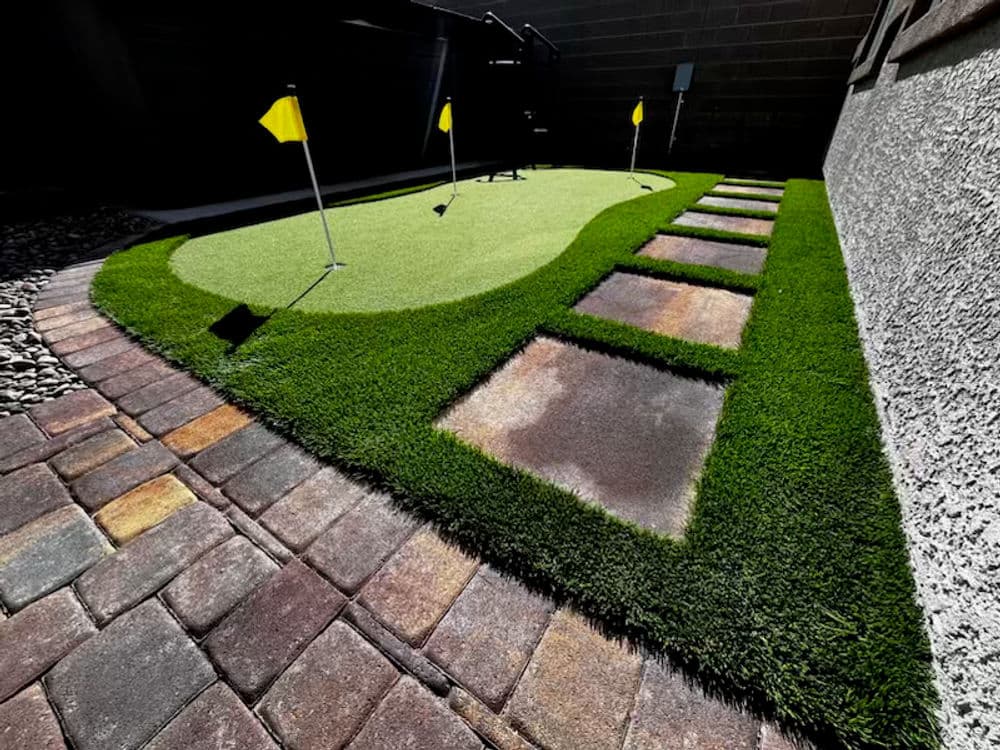 Backyard putting green with yellow flags and stone pathway bordered by artificial grass.