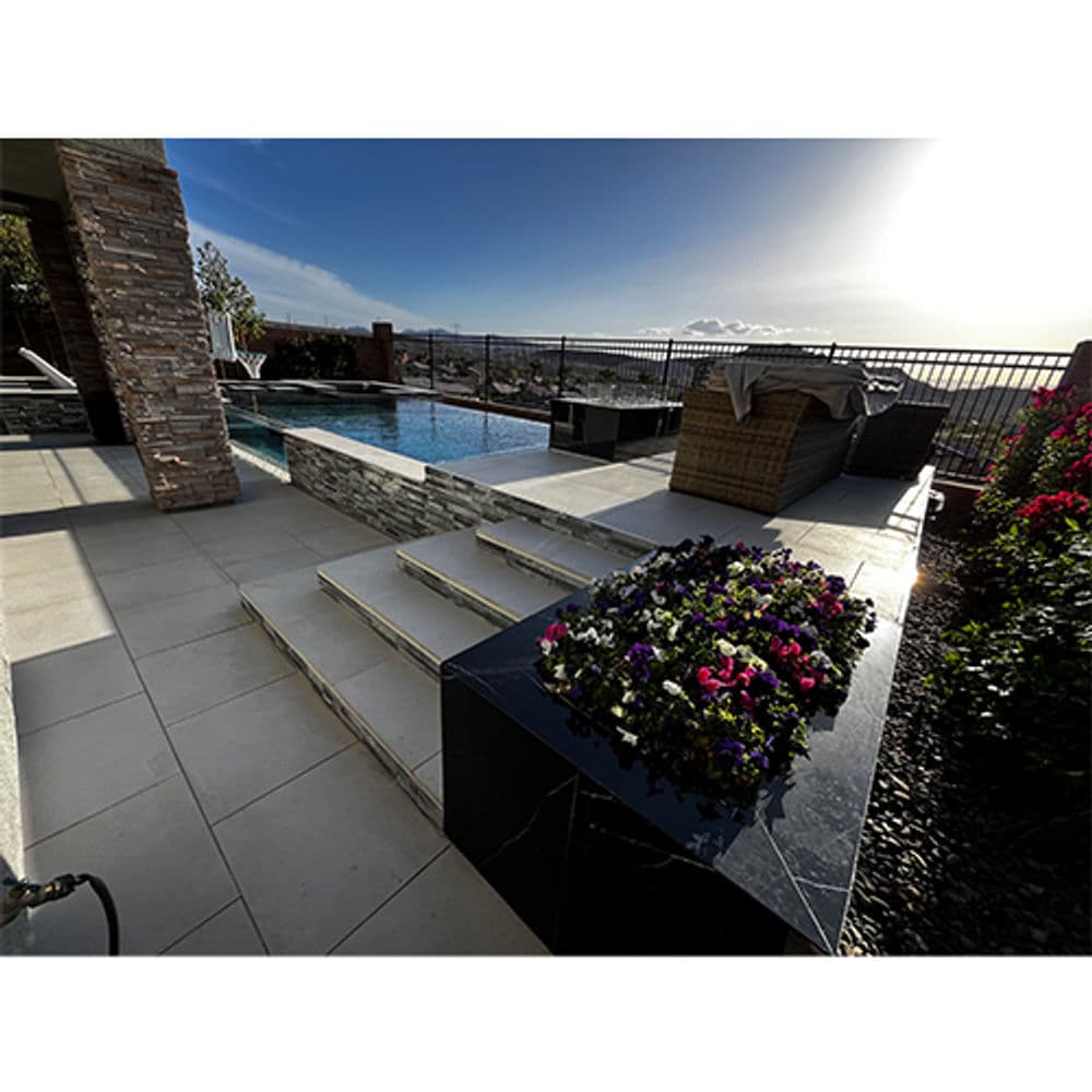 Modern patio with a pool, stone features, and vibrant flower beds, overlooking a scenic view.