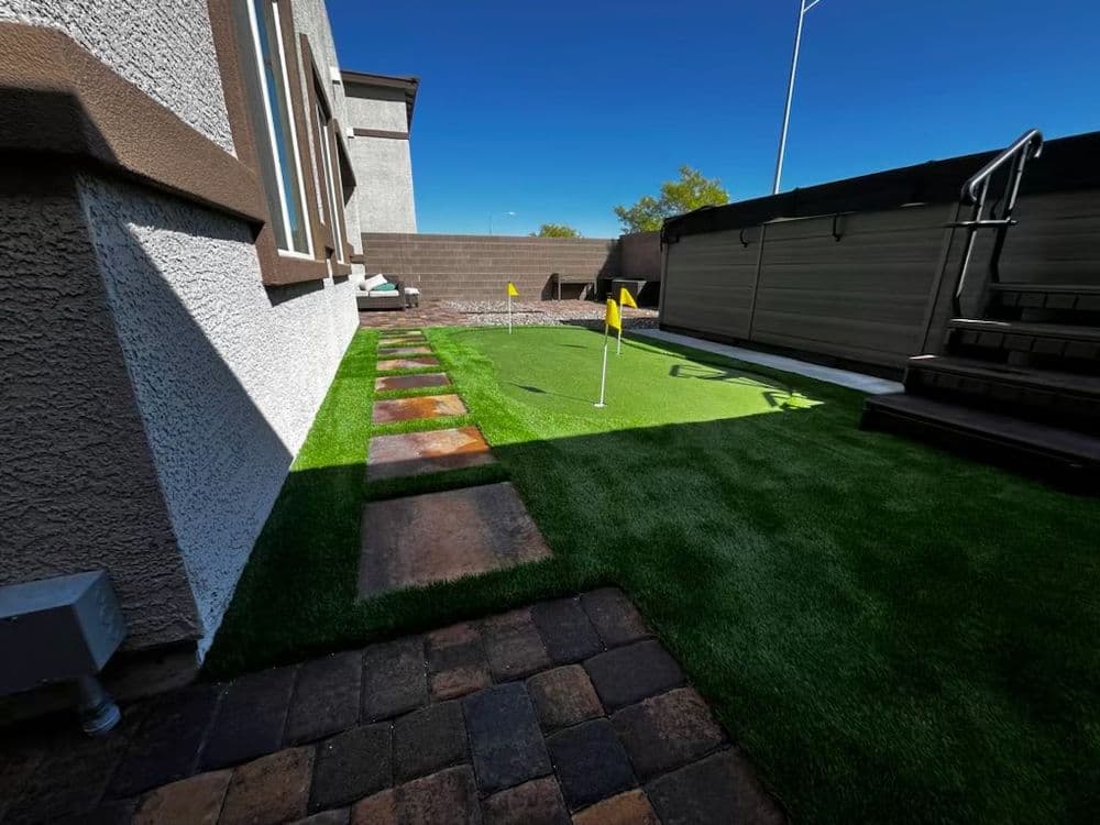 Lush backyard putting green with flag, stone pathway, and modern home exterior.