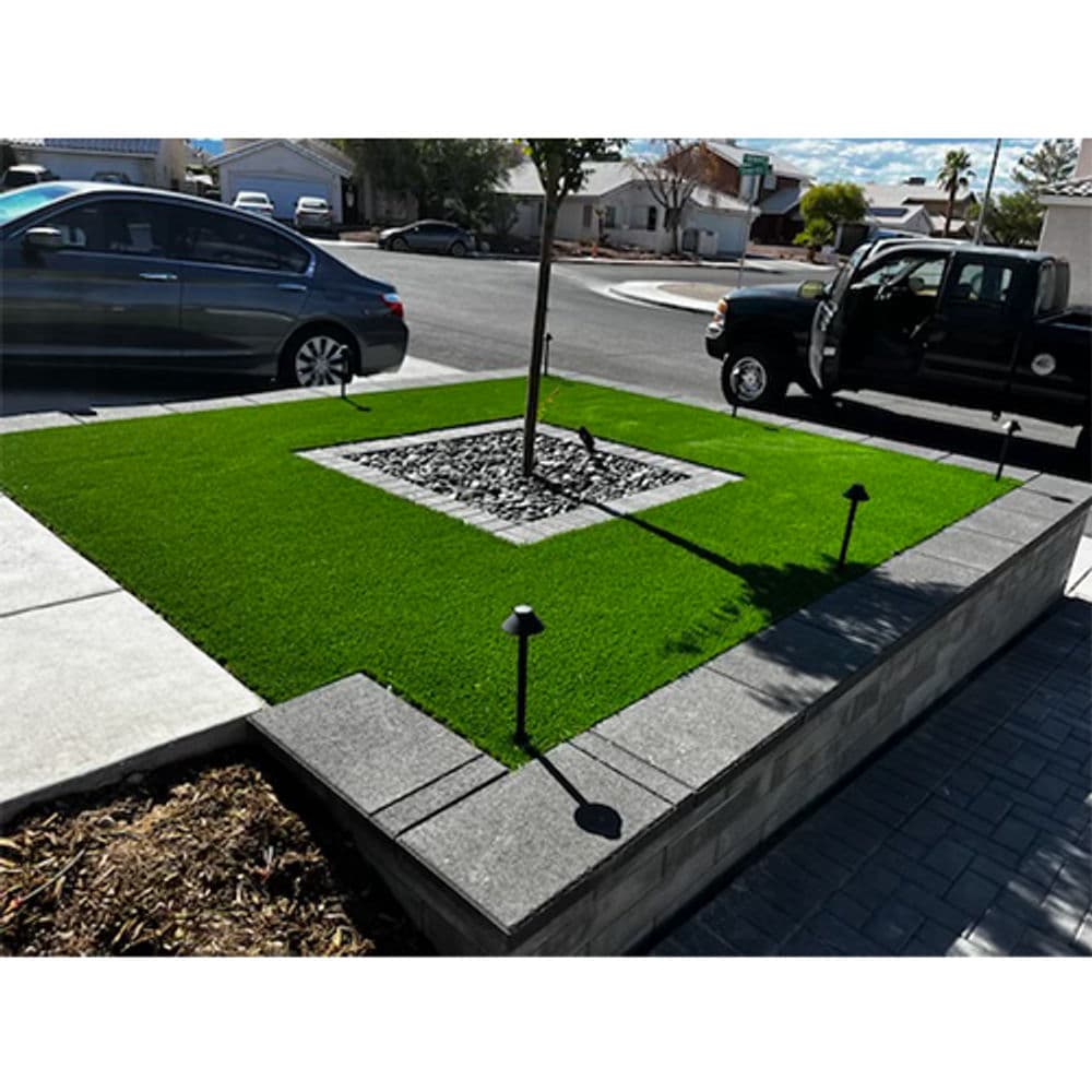 Lush green artificial turf landscape with stone centerpiece and cars parked nearby.