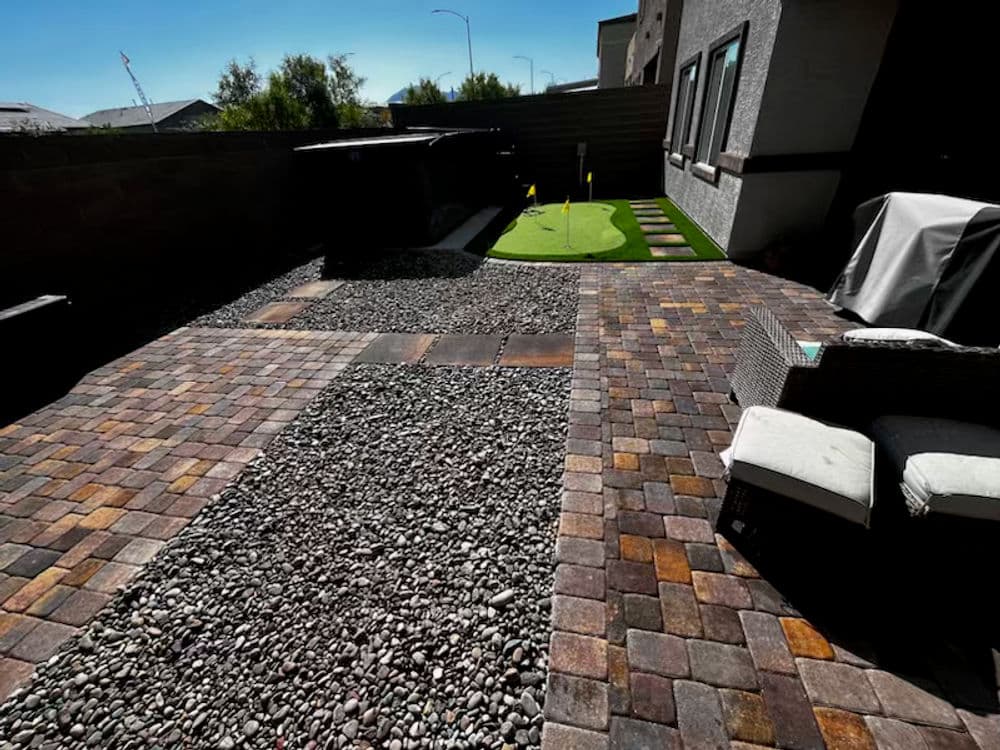 Stylish backyard features paver stone pathways, gravel area, and putting green.
