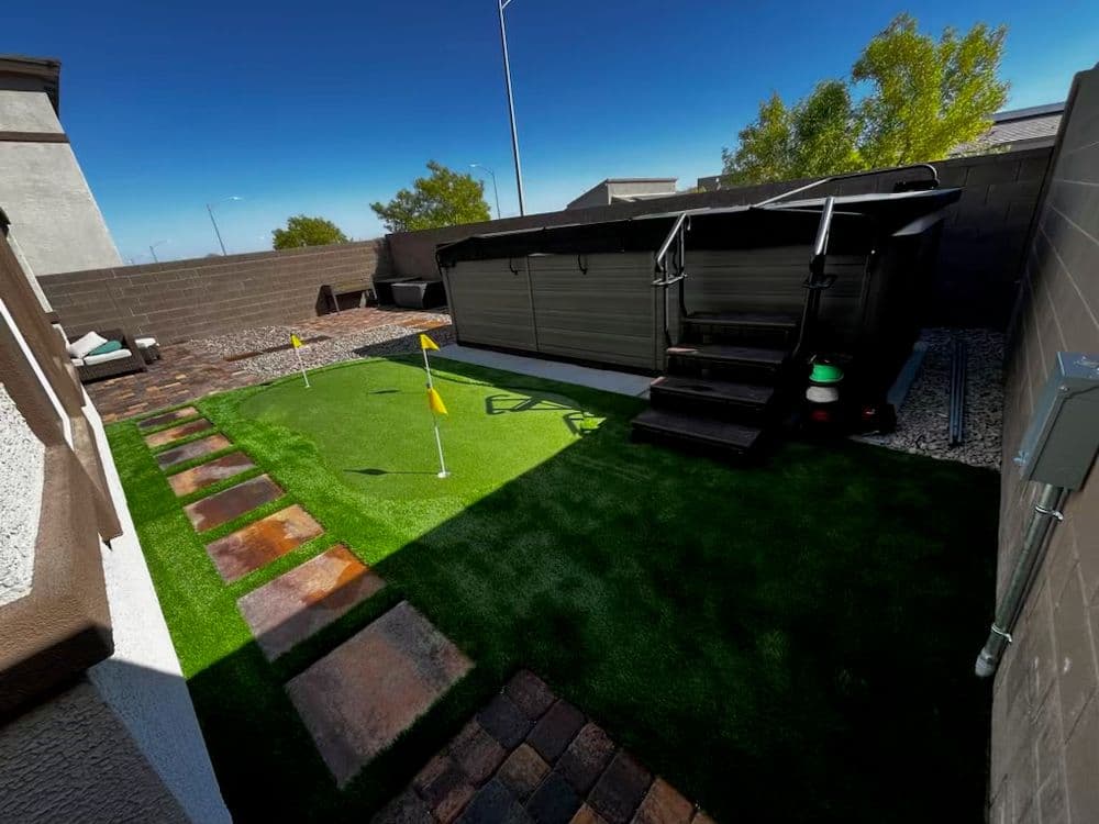 Backyard putting green with turf, decorative stones, and a shaded lounge area.