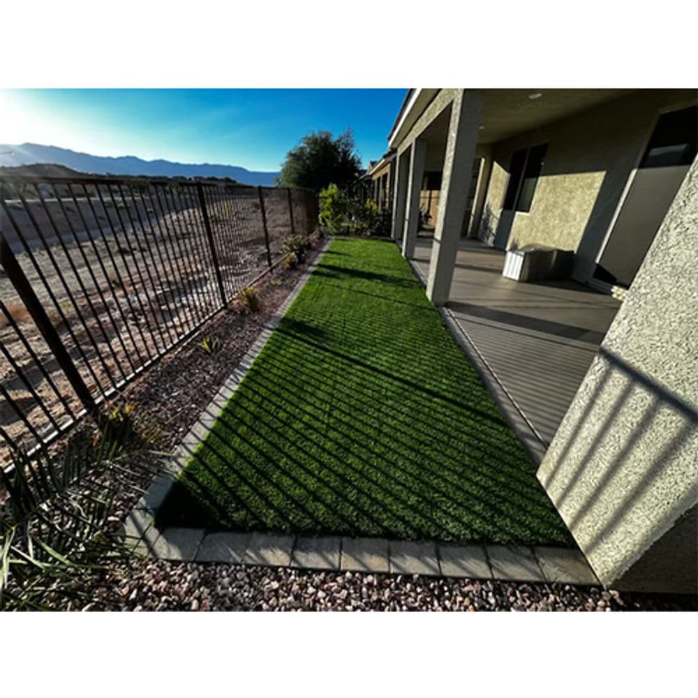 Lush green artificial turf beside a home, surrounded by a fence and desert landscape.