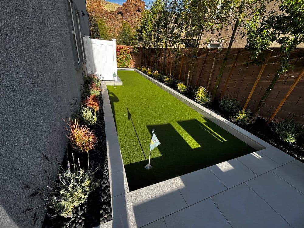 Modern backyard putting green surrounded by low-maintenance landscaping and stone features.