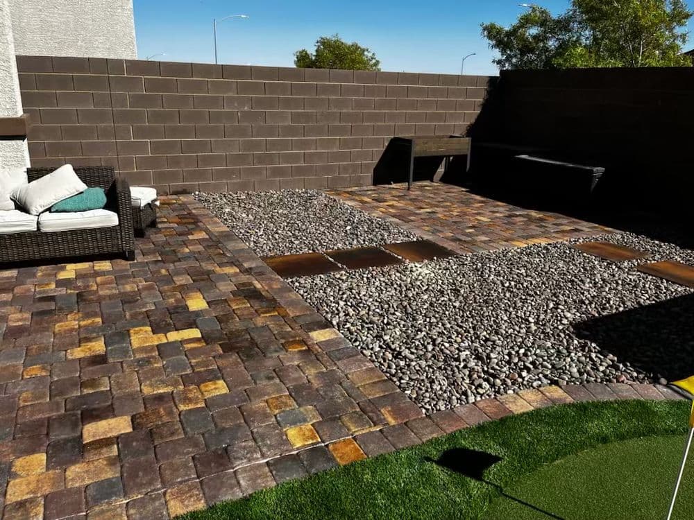 Modern outdoor patio with stone pavers, gravel, and seating in a sunny, landscaped setting.