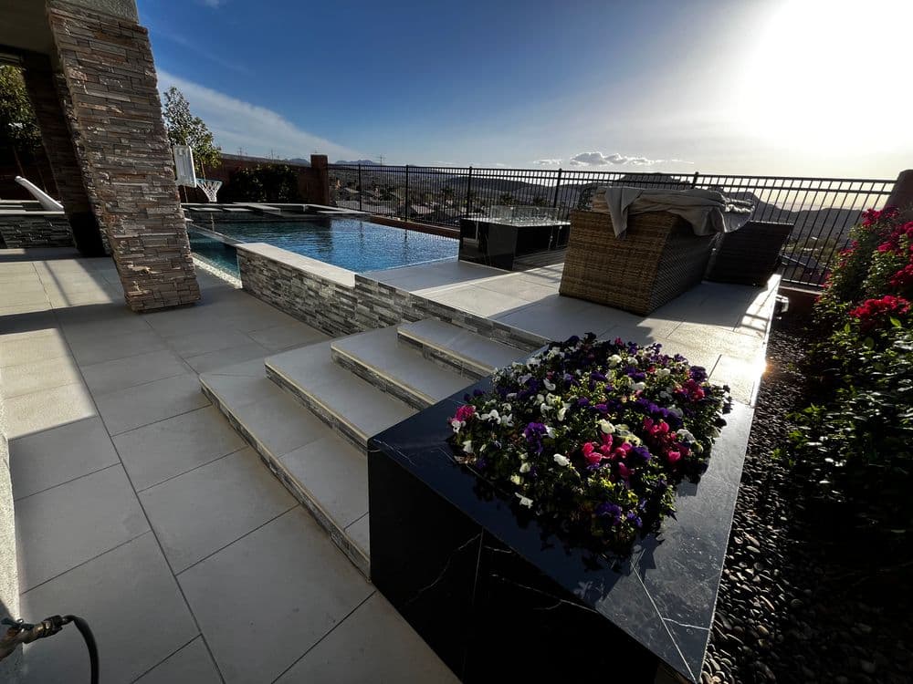 Elegant outdoor patio with a pool, stone wall, and colorful flower arrangement under bright skies.