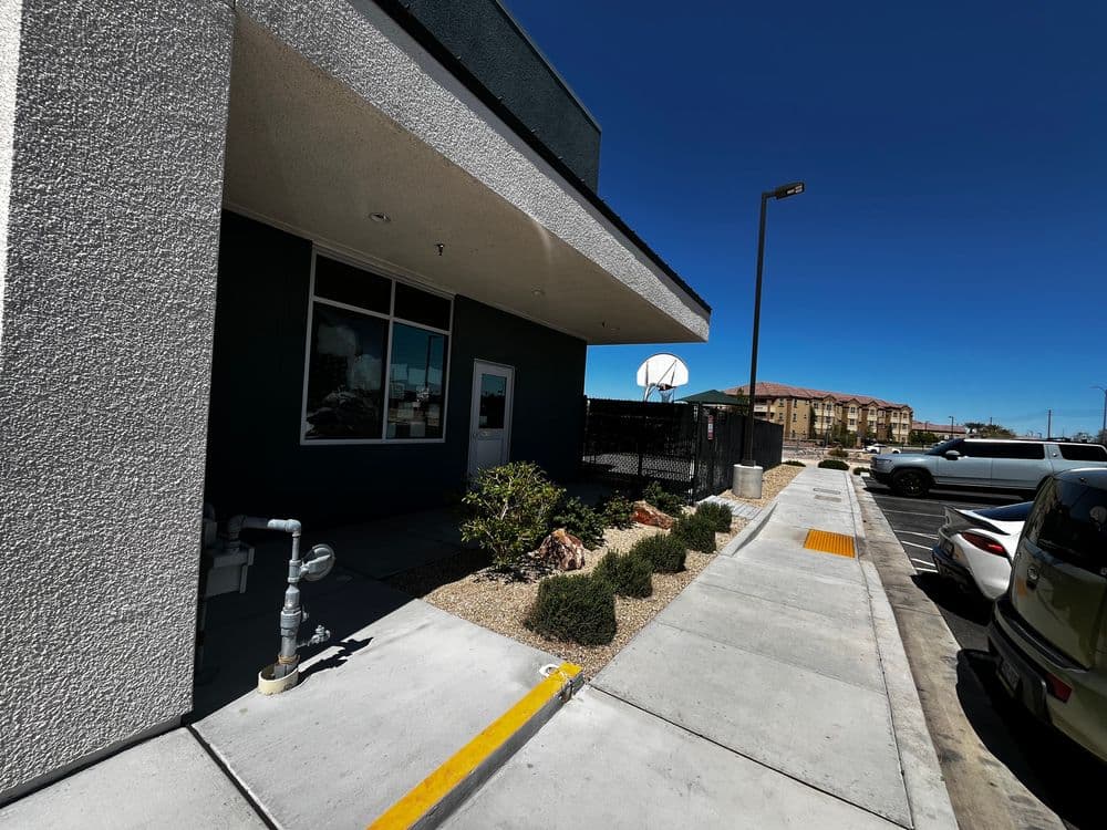 Exterior of a modern building with basketball hoop, parking lot, and landscaping. Clear blue sky.