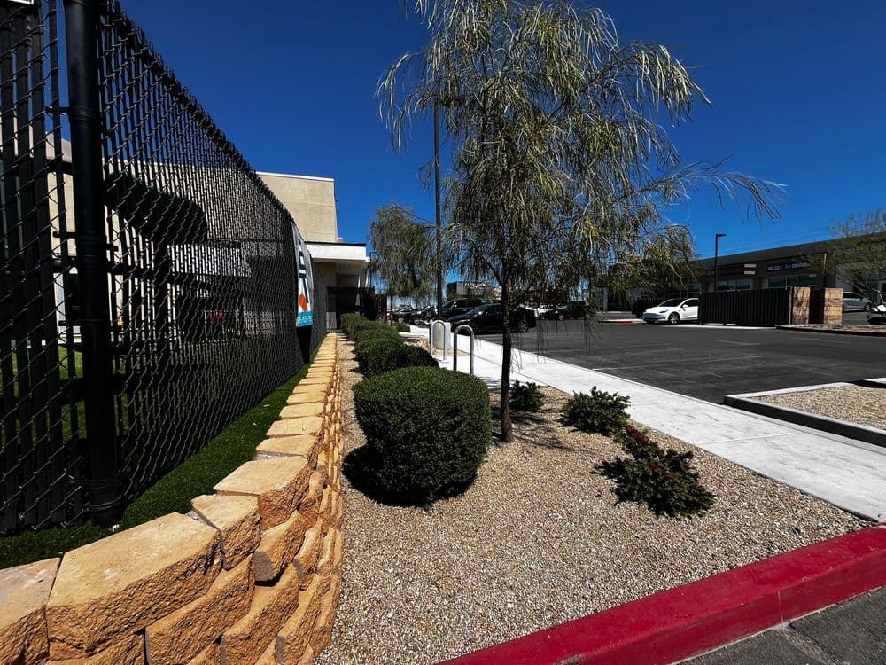 Landscaped exterior with fencing and parking lot near a commercial building. Clear blue sky.